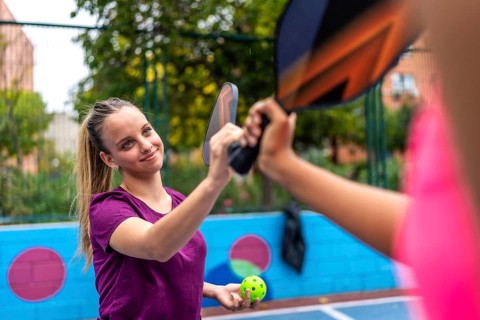 Smiling sportive blonde woman shaking racket with partner in a pickelball court