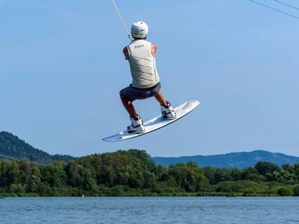 Young man jumping with wakeboard over jump and obstacle, water sports, water skiing in wakepark,