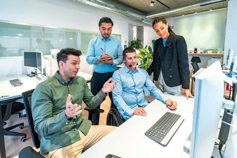 Diverse business team collaborating on a computer project, demonstrating inclusion and teamwork in