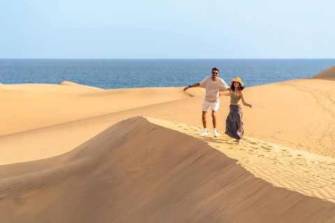 Couple running down sand dunes at maspalomas with ocean in background enjoying summer vacation in