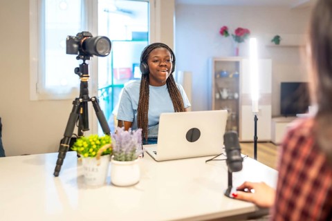 Two young content creators recording a podcast or video using a laptop, microphone, camera, and