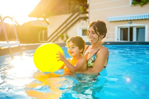 Mother and son having fun together in a home swimming pool, playing with a yellow inflatable ball