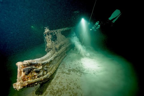 Underwater image of a diver approaching a shipwreck with a light source, dive site wreck of the