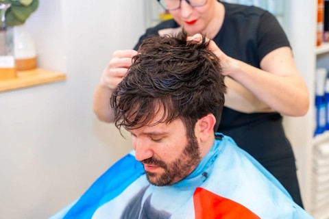 Hairstylist attaching a new capillary prosthesis to a man's head sitting on a salon