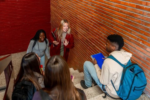 Multi ethnic students walking down the stairs and greeting a classmate sitting on the steps
