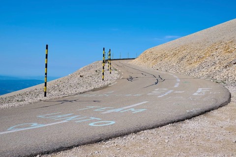 Winding road on a barren hill under a clear blue sky with yellow posts at the edge, Mont Ventoux,