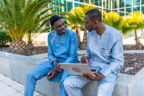 Two senegalese businessmen wearing traditional dashiki attire are discussing business while using a