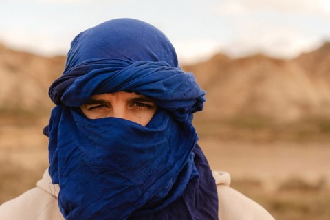 Portrait of a tuareg man adorned in an indigo tagelmust, set against the vast, arid landscape of