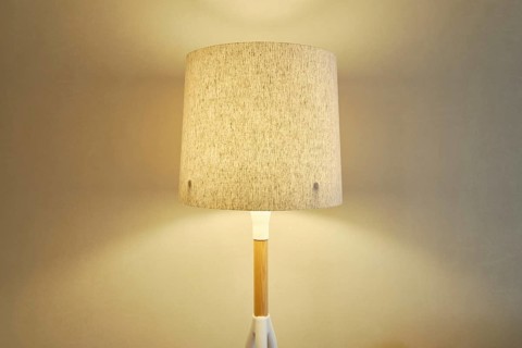 A stylish lamp with a beige fabric shade casting a soft warm light on the wall in the room