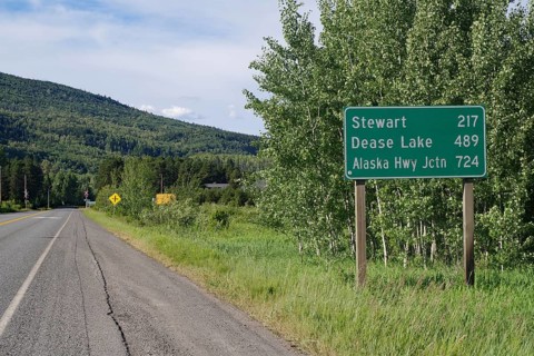 Narrow, traffic-free road leads through forest landscape, sign with huge distances, wilderness,