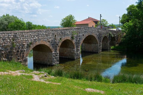 Stone bridge over river, flanked by green bank and small building, Bridge over the river Zrmanja,