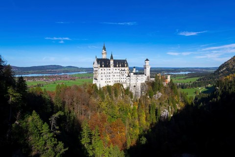 Panoramic view of Neuschwanstein surrounded by autumnal trees and mountains, Schwangau, Ostallgäu,