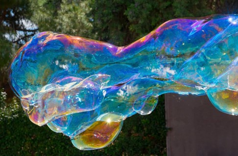 Large, brightly coloured soap bubble floats in front of a wooded background, Spain