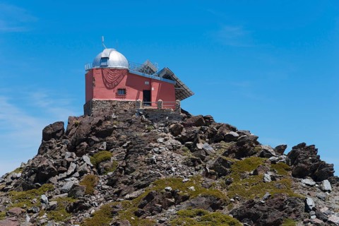 Close-up of a red observatory on a rocky hill under a blue sky, Obversatorium, Mohon del Trigo