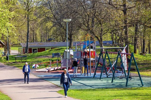 Playground in a public park with children playing and people walking on a footpath at springtime,