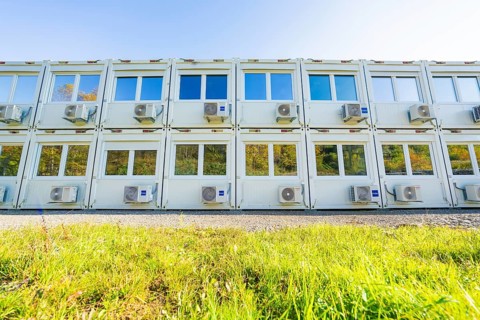 Several white containers with windows and air conditioning units stand on a green meadow, Beermiß