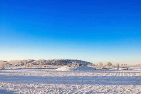 Winter landscape with snow and frost in the countryside with a Passage grave on a hill and a table