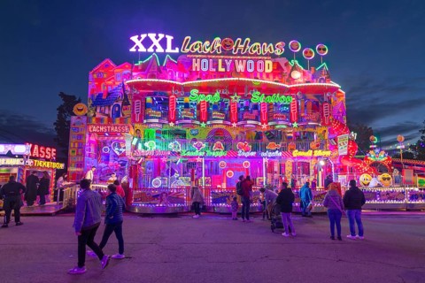 Colourfully illuminated fun house at a funfair at night with numerous visitors, Cannstatter Wasen,