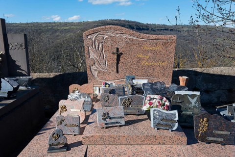 Grabsteine und Blumenschmuck auf einem Friedhof in einer hügeligen Landschaft mit einem