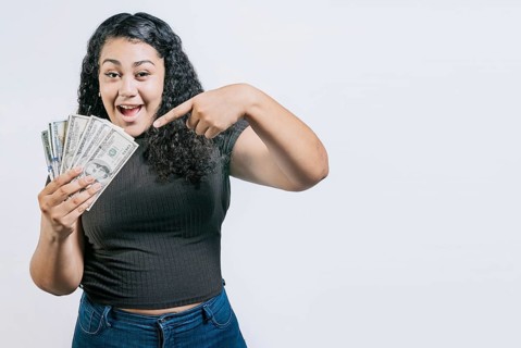 Smiling young woman holding and pointing money isolated. Attractive latin girl holding and pointing