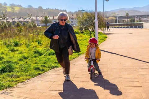 Grandmother jogging behind her grandson riding a balance bike in a park, having fun together on a