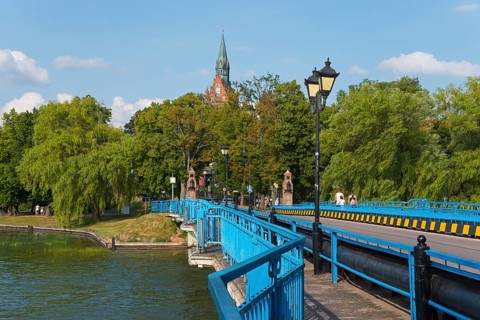 Blue bridge against a lush green backdrop with church tower and lanterns in sunny weather, historic