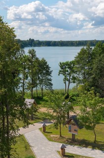 Lake with surrounding trees and well-kept path under a blue sky with clouds, view from the