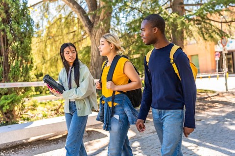 Side view of three multi-ethnic friends walking out the university campus