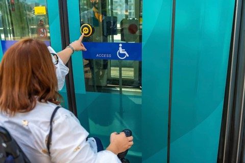 Woman using a wheelchair is pushing accessible button to enter public transport, promoting