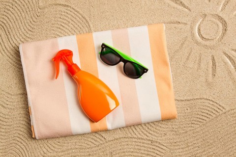 Drawing on the sand, sun and waves, sunglasses, with an orange bottle, beach towel, sun spray, on
