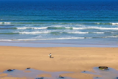 Man with a surfboard walking up from the water with breaking waves on a sand beach, Crozon