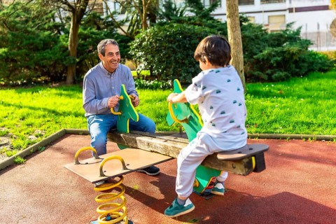 Grandfather and grandson enjoying a sunny day together at the park, playing joyfully on a seesaw,