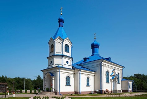 Orthodox church with a blue roof and white facades under a clear sky in a summer landscape,