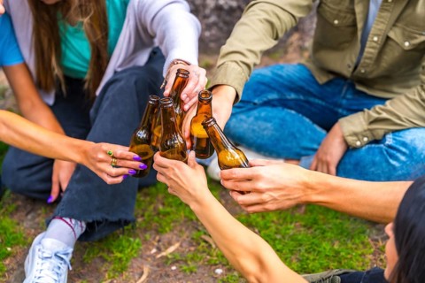 Group of multi-ethnic friends sitting in the city park talking next to a tree with bottles of beers