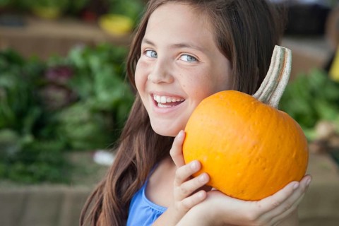 Happy young blue eyed girl holding a fresh pumpkin at the farmers market