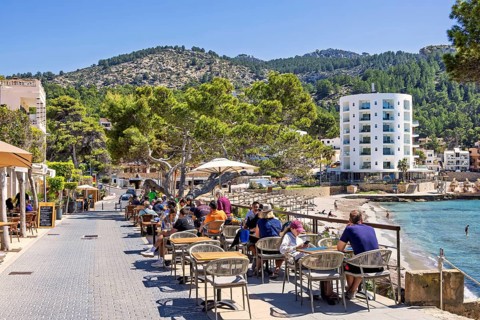 Outdoor restaurant with people on a pedestrian street in a coastal village by the beach with hotels