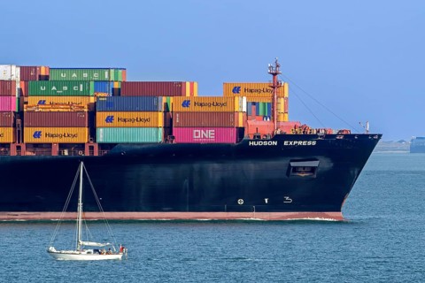 Sailboat sailing past bow of container ship, containership Hudson Express of the Hapag-Lloyd AG