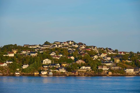Small wooded island with houses in the sea with clear skies and calm water, Strusshamn, Bergen,