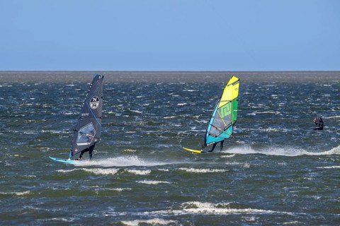 Kiteboarder, kitesurfer and two recreational windsurfers in wetsuits practising classic windsurfing