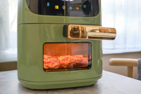 A fresh pork chop is being cooked in an air fryer, showcasing its sleek green design. The appliance