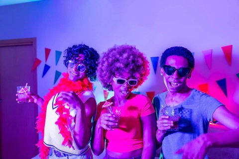 Multiracial friends partying at home at night with colorful neon light illuminating the apartment