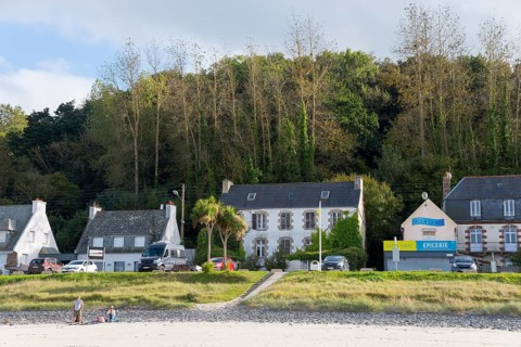 Beach view with houses and shops on the coast, surrounded by green trees, Plage Saint Efflamm,