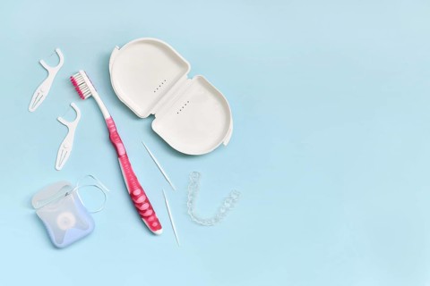 Top view of dental clear aligners, toothbrush, toothpicks and floss on blue background with copy