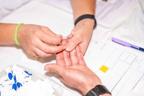 Close-up of a nurse checking blood sugar level by pricking the finger of a blood donor
