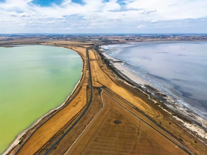 Aerial photo contrasting vibrant green and gray lakes divided by roads and golden fields in