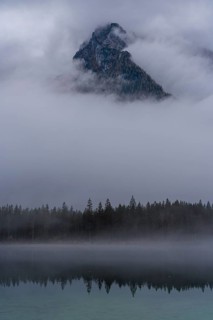 A stunning view of a mountain peak in Hintersee, partially shrouded in fog, surrounded by serene