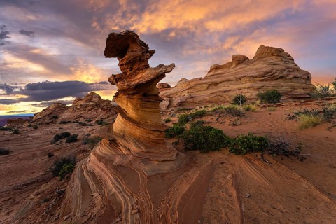 A stunning sunset casts warm hues over the distinctive swirls and layers of sandstone rock