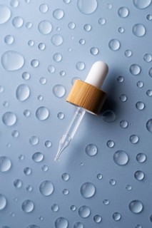 A glass pipette bottle lies on a textured blue surface Water droplets surround the bottle,