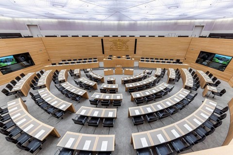 Plenary hall deserted with the seats of deputies and the government bank. Behind it is the coat of