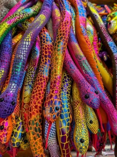 A vibrant collection of colorful plush snakes displayed in a Thai souvenir market. Each snake